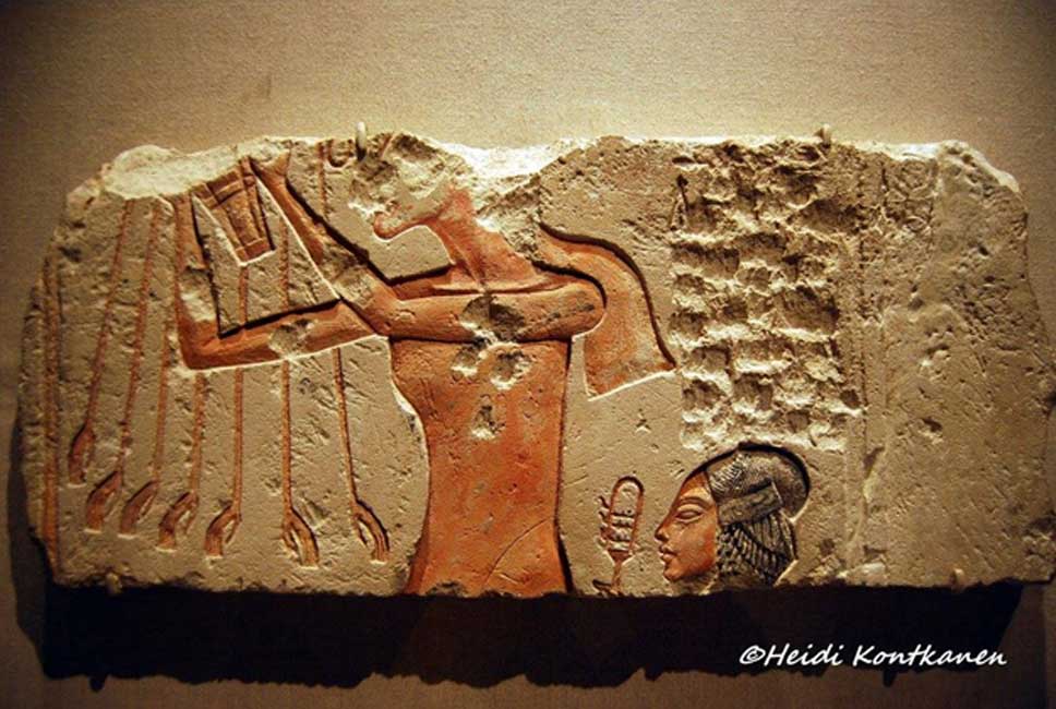 A painted limestone block from Tell el-Amarna shows Akhenaten presenting a bouquet to the Aten; while his daughter, Meritaten, who wears her hair in an elaborate plaited sidelock symbolizing youth, shakes a sistrum. Brooklyn Museum, New York.