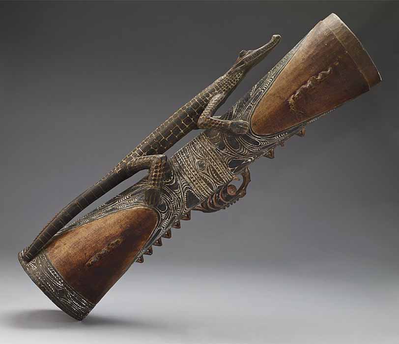 Kundu drum, an hourglass shaped drum made of wood, and normally covered with a snake or lizard's skin as membrane. The crocodile is symbolic to the Iatmul people. There are three crocodiles on this instrument: the handle and each of the drum openings (Public Domain)